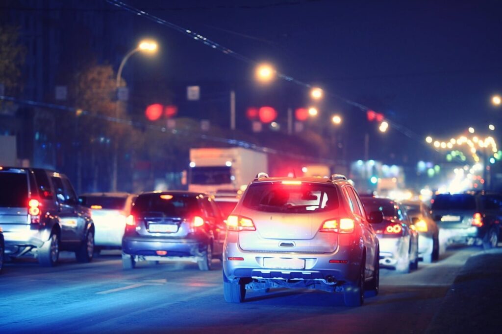 Cars are stopped in heavy nighttime traffic on a city street, with headlights and brake lights illuminating the scene.
