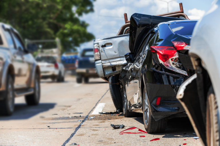 A black car and a white pickup truck involved in a rear-end collision on a busy road, with visible damage and debris on the pavement.