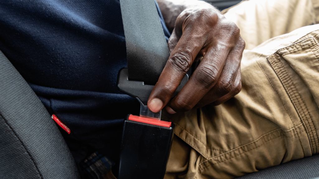 Close-up of a person wearing tan pants and a navy shirt fastening a seat belt in a car.