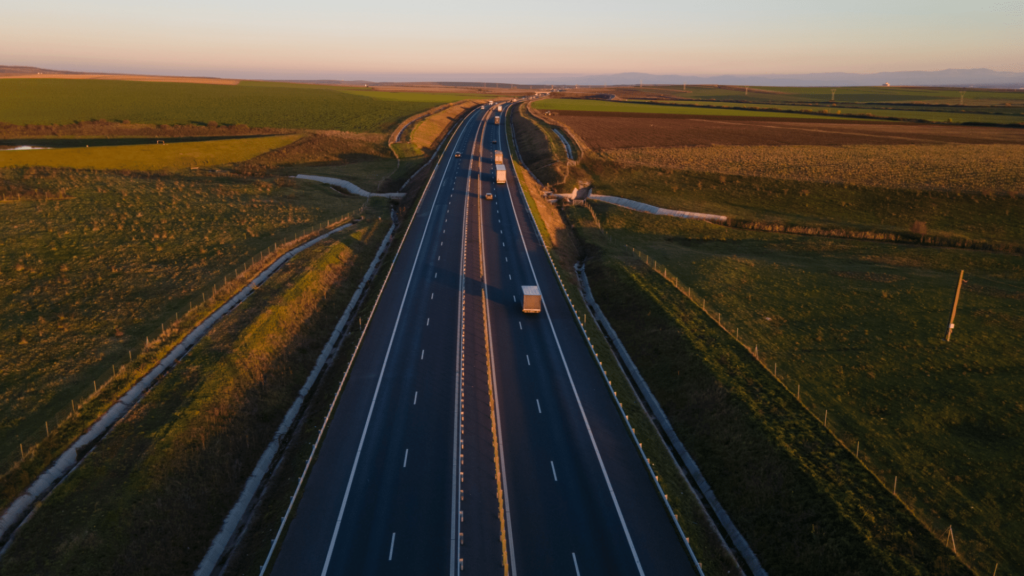 Aerial view of a highway with several vehicles traveling in both directions, surrounded by green fields at sunset.
