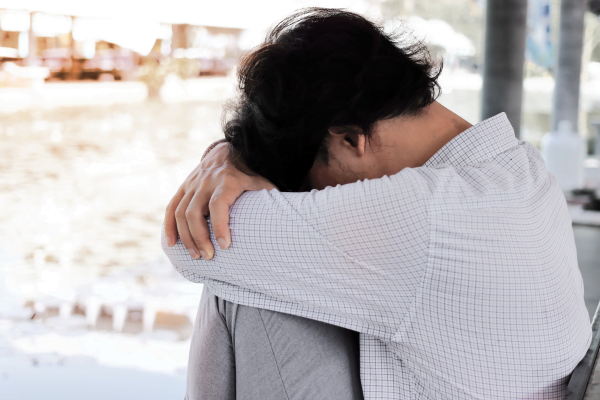 A person sits with knees drawn up and head resting on arms, appearing to be in distress or deep thought.