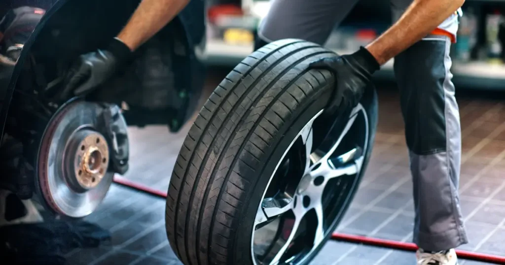 A person wearing gloves is removing a car tire next to a brake disc in an auto repair shop.