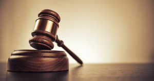 A wooden judge’s gavel rests on its sound block against a brown background.