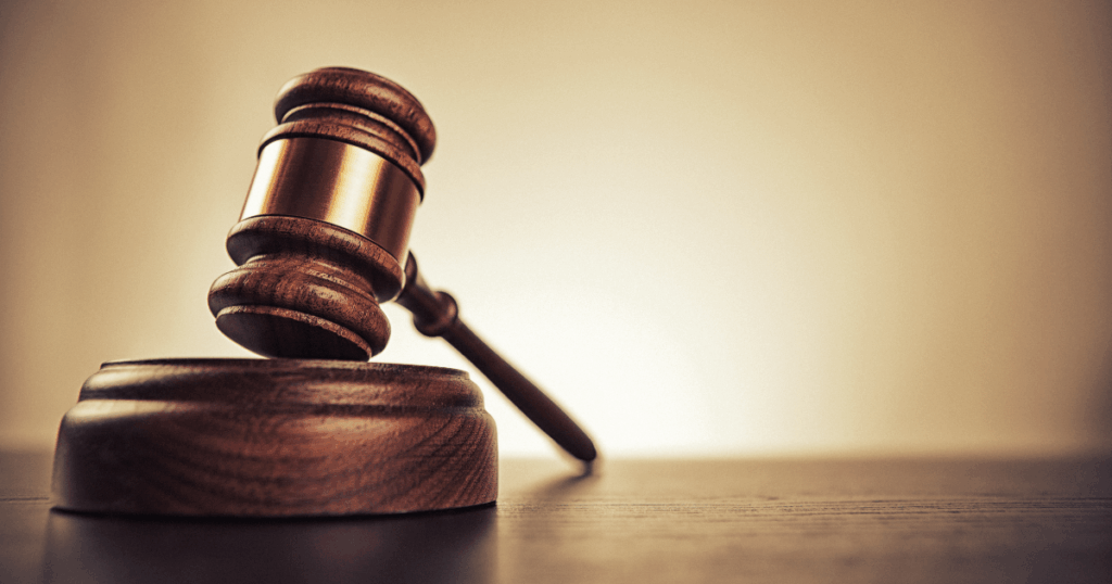 A wooden judge’s gavel rests on its sound block against a brown background.